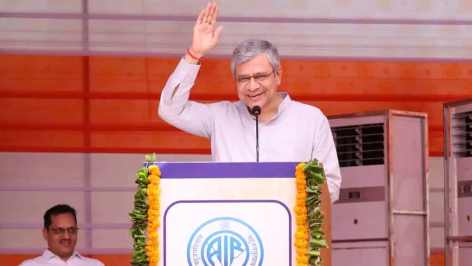 तस्वीर में पोडियम के पीछे माइक के सामने खड़े मुस्कुराते हुए केंद्रीय मंत्री अश्विनी वैष्णव जैसलमेर के रामगढ़ में एफएम ट्रांसमीटर के वर्चुअल उद्घाटन समारोह के संदर्भ में दिख रहे हैं। तस्वीर में पोडियम के पीछे माइक के सामने खड़े मुस्कुराते हुए केंद्रीय मंत्री अश्विनी वैष्णव जैसलमेर के रामगढ़ में एफएम ट्रांसमीटर के वर्चुअल उद्घाटन समारोह के संदर्भ में दिख रहे हैं।