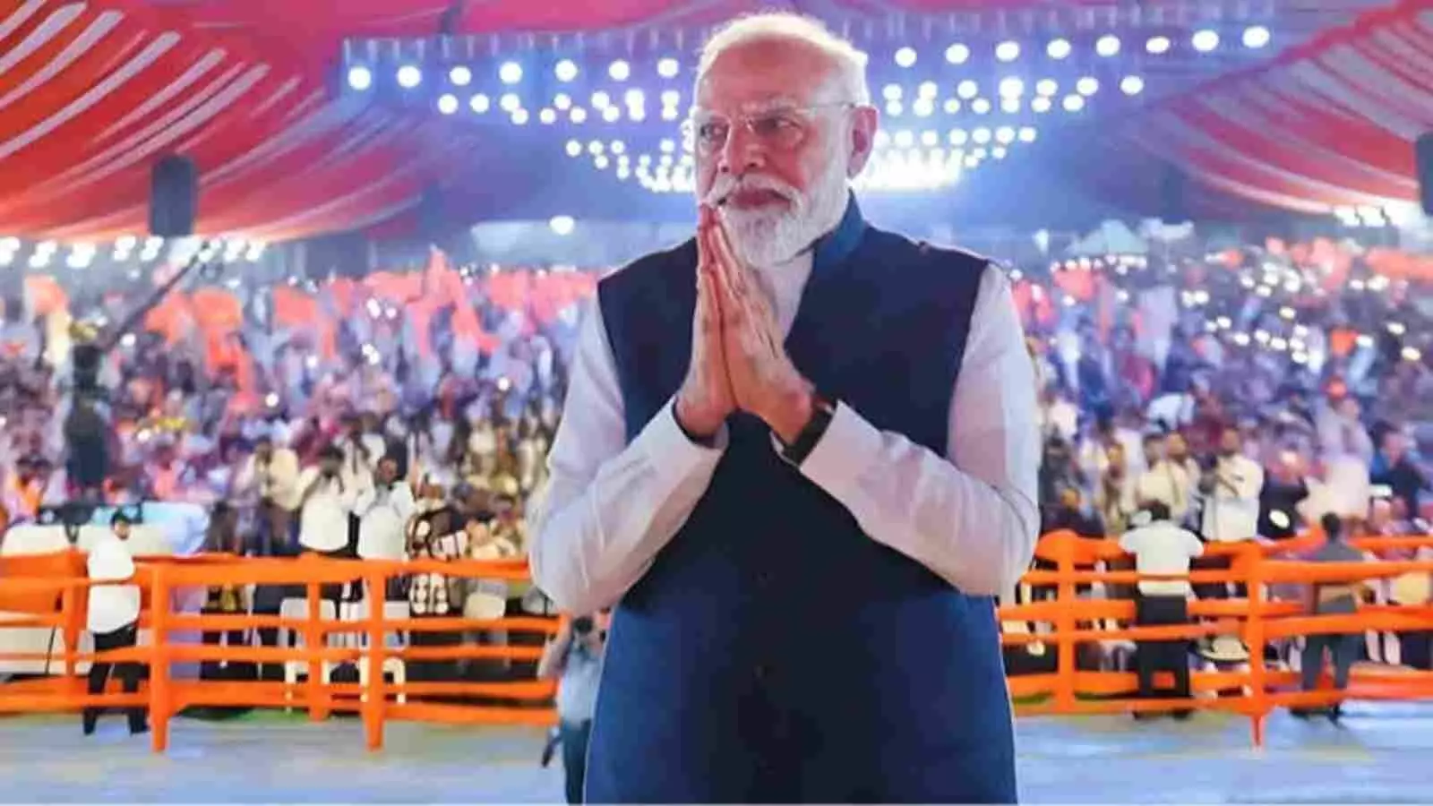 मंच पर हाथ जोड़कर खड़े प्रधानमंत्री नरेंद्र मोदी पृष्ठभूमि में उपस्थित जनसमूह के सामने। मंच पर हाथ जोड़कर खड़े प्रधानमंत्री नरेंद्र मोदी पृष्ठभूमि में उपस्थित जनसमूह के सामने।