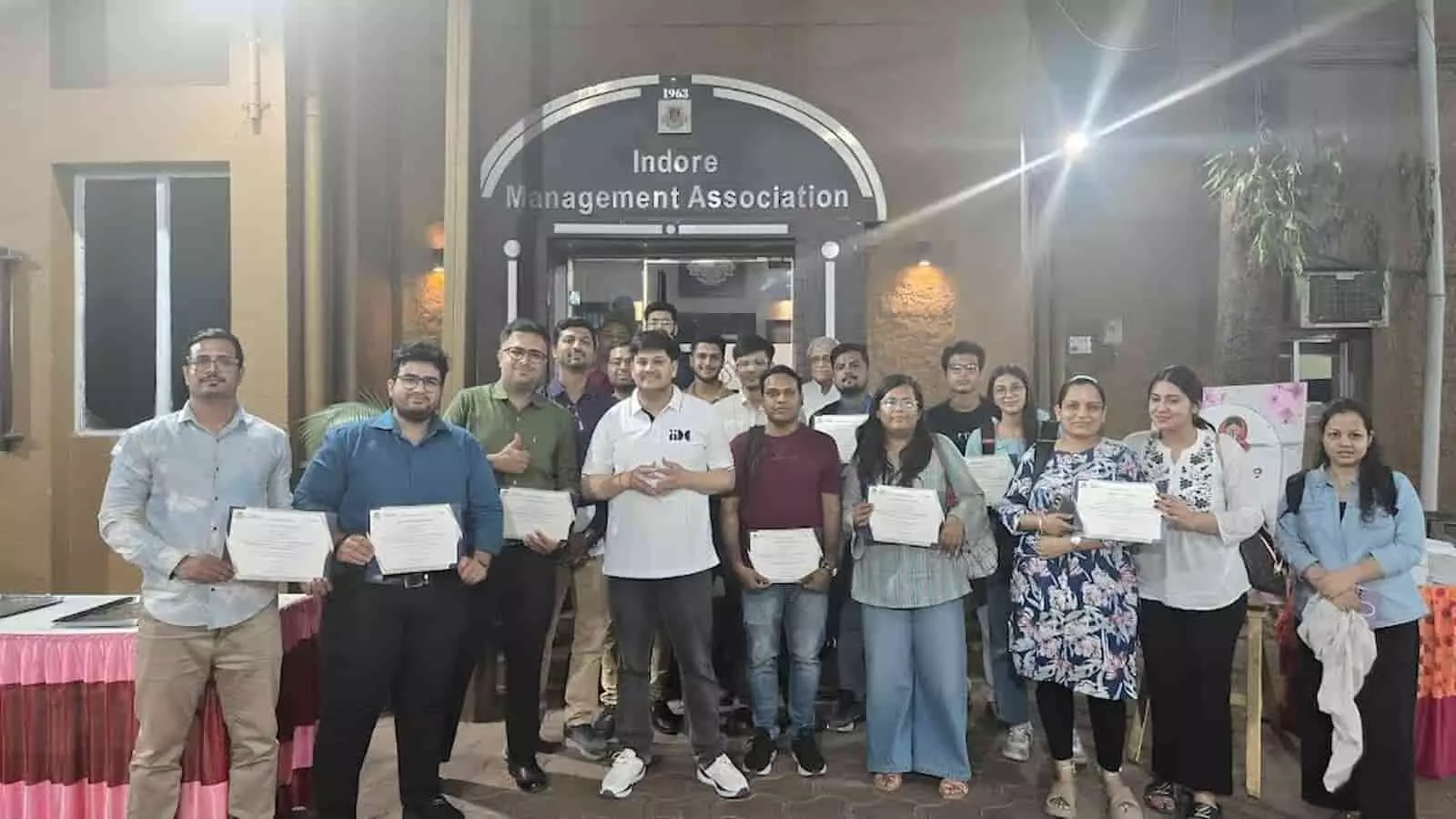 तस्वीर में कई युवा और पेशेवर प्रतिभागी इंदौर मैनेजमेंट एसोसिएशन भवन के मुख्य प्रवेश द्वार के सामने खड़े होकर अपने हाथों में सहभागिता प्रमाण-पत्र प्रदर्शित कर रहे हैं।