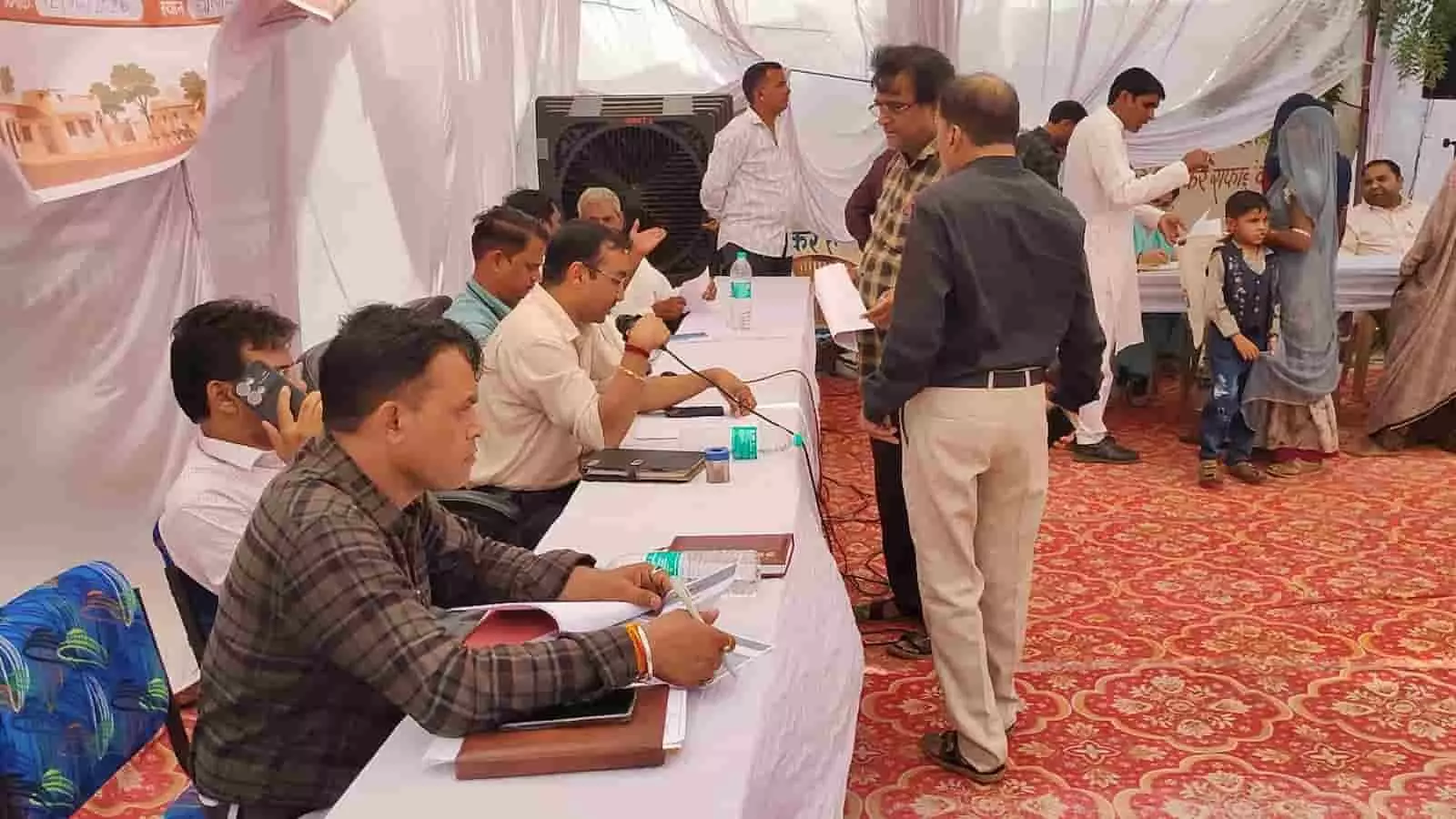 धोलापानी ग्राम पंचायत के ग्रामीण सेवा शिविर में जमीन पर बैठीं ग्रामीण महिलाएं और अधिकारी। धोलापानी ग्राम पंचायत के ग्रामीण सेवा शिविर में जमीन पर बैठीं ग्रामीण महिलाएं और अधिकारी।