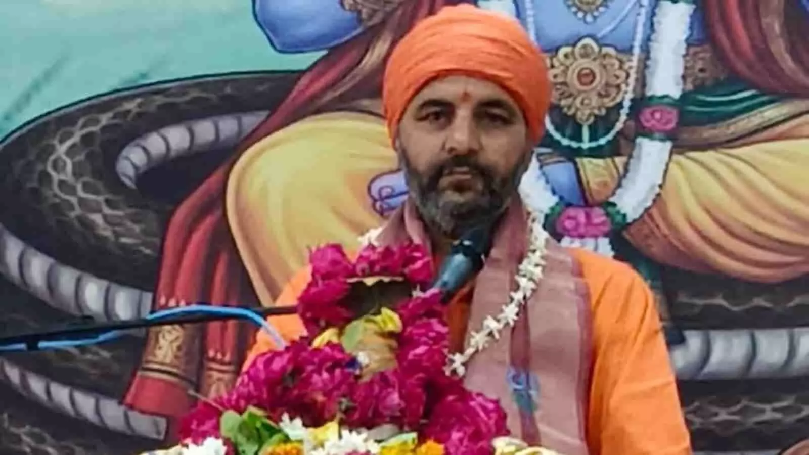 तस्वीर में केसरिया रंग का कुर्ता और सिर पर केसरिया पगड़ी (साफा) पहने एक दाढ़ी वाले संत माइक के सामने बैठे हुए दिखाई दे रहे हैं। तस्वीर में केसरिया रंग का कुर्ता और सिर पर केसरिया पगड़ी (साफा) पहने एक दाढ़ी वाले संत माइक के सामने बैठे हुए दिखाई दे रहे हैं।