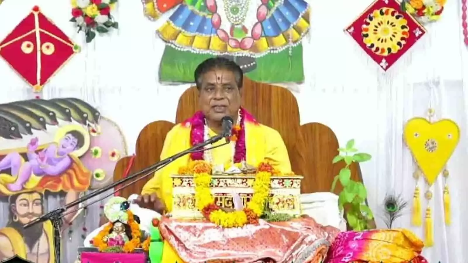तस्वीर में एक सुसज्जित धार्मिक मंच (व्यासपीठ) पर फूलों की माला पहने एक कथावाचक बैठे हुए हैं और उनके सामने माइक व धार्मिक ग्रंथ रखे हैं। तस्वीर में एक सुसज्जित धार्मिक मंच (व्यासपीठ) पर फूलों की माला पहने एक कथावाचक बैठे हुए हैं और उनके सामने माइक व धार्मिक ग्रंथ रखे हैं।