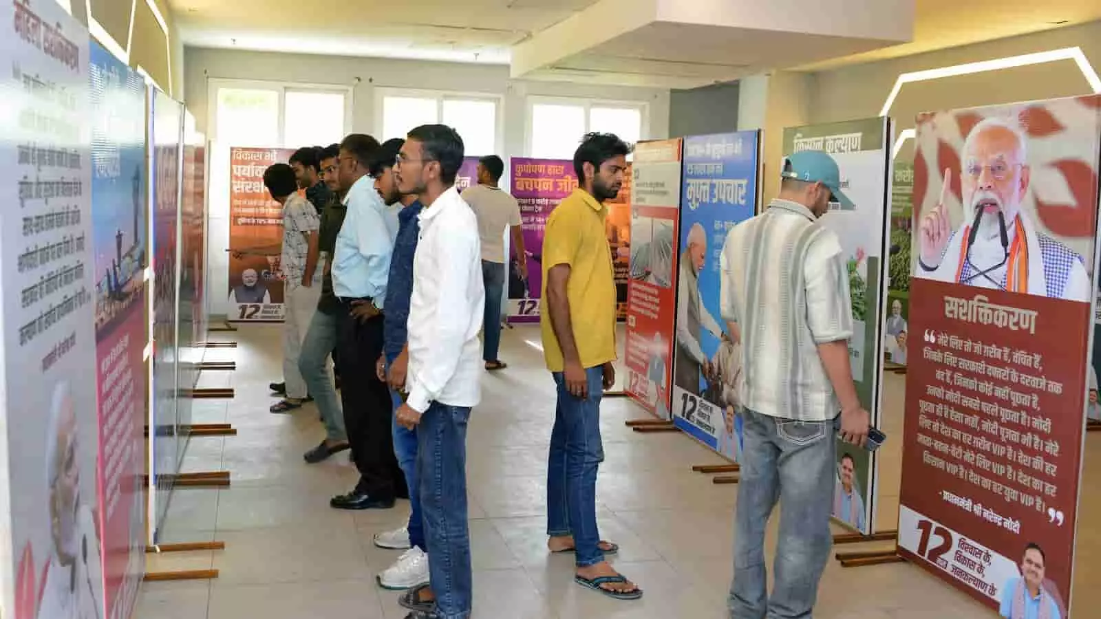 तस्वीर में एक प्रदर्शनी हॉल के भीतर कई लोग दीवारों और बोर्ड पर लगी विकास योजनाओं की जानकारियों को पढ़ते हुए दिख रहे हैं।