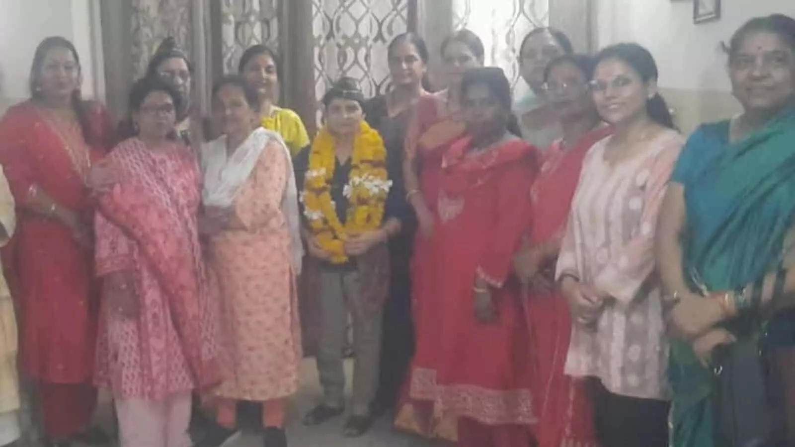 तस्वीर में एक कमरे के भीतर कई महिलाएं एक साथ खड़ी हुई हैं जिसमें बीच में खड़ी एक महिला के गले में गेंदे के फूलों की माला दिख रही है। तस्वीर में एक कमरे के भीतर कई महिलाएं एक साथ खड़ी हुई हैं जिसमें बीच में खड़ी एक महिला के गले में गेंदे के फूलों की माला दिख रही है।