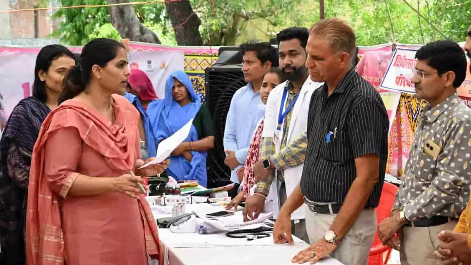 तस्वीर में एक शिविर के खुले पंडाल के नीचे टेबल के पास खड़ीं महिला प्रशासनिक अधिकारी हाथ में कागज थामे कुछ लोगों से चर्चा करती हुई दिख रही हैं। तस्वीर में एक शिविर के खुले पंडाल के नीचे टेबल के पास खड़ीं महिला प्रशासनिक अधिकारी हाथ में कागज थामे कुछ लोगों से चर्चा करती हुई दिख रही हैं।