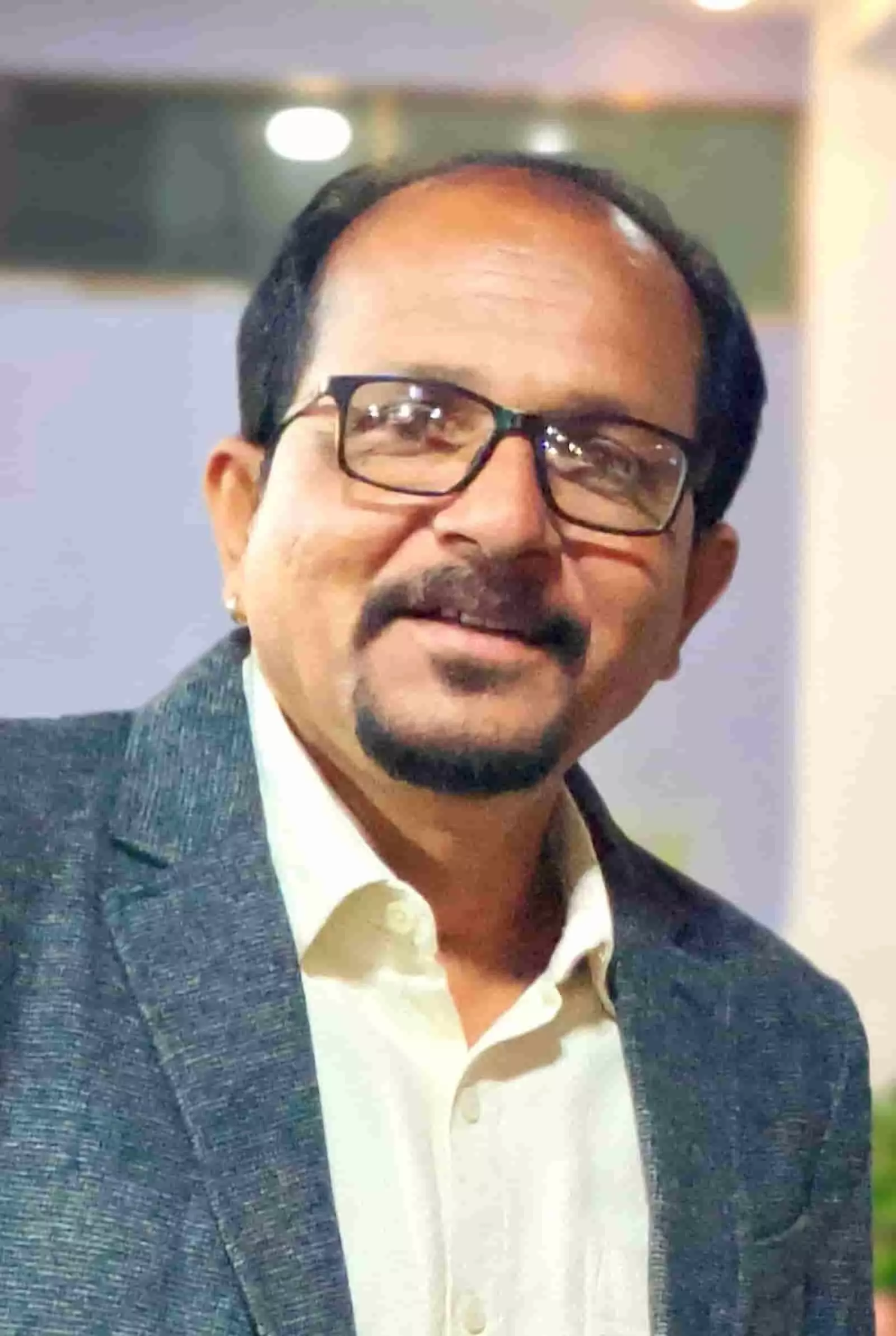 तस्वीर में चश्मा और दाढ़ी-मूंछ रखे एक व्यक्ति सूट-शर्ट पहने हुए कैमरे के सामने मुस्कुराते हुए दिखाई दे रहे हैं। तस्वीर में चश्मा और दाढ़ी-मूंछ रखे एक व्यक्ति सूट-शर्ट पहने हुए कैमरे के सामने मुस्कुराते हुए दिखाई दे रहे हैं।
