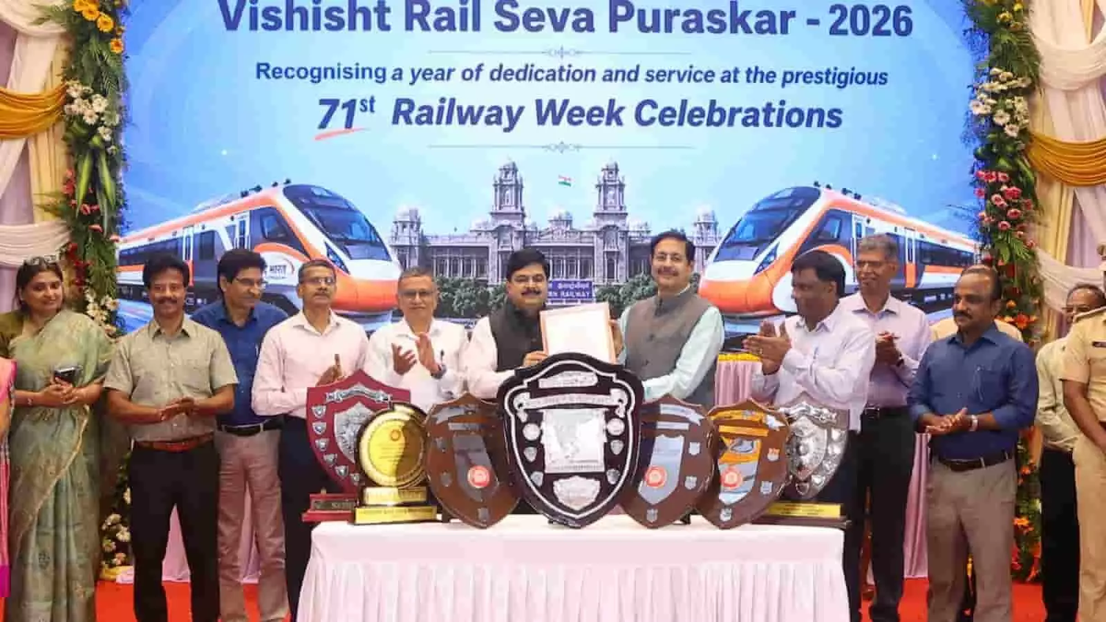 तस्वीर में एक बड़े बैकड्रॉप के सामने खड़े कई रेल अधिकारी टेबल पर सजीं बड़ी-बड़ी शील्ड और ट्रॉफी के पीछे खड़े होकर मुस्कुराते और ताली बजाते दिख रहे हैं। तस्वीर में एक बड़े बैकड्रॉप के सामने खड़े कई रेल अधिकारी टेबल पर सजीं बड़ी-बड़ी शील्ड और ट्रॉफी के पीछे खड़े होकर मुस्कुराते और ताली बजाते दिख रहे हैं।