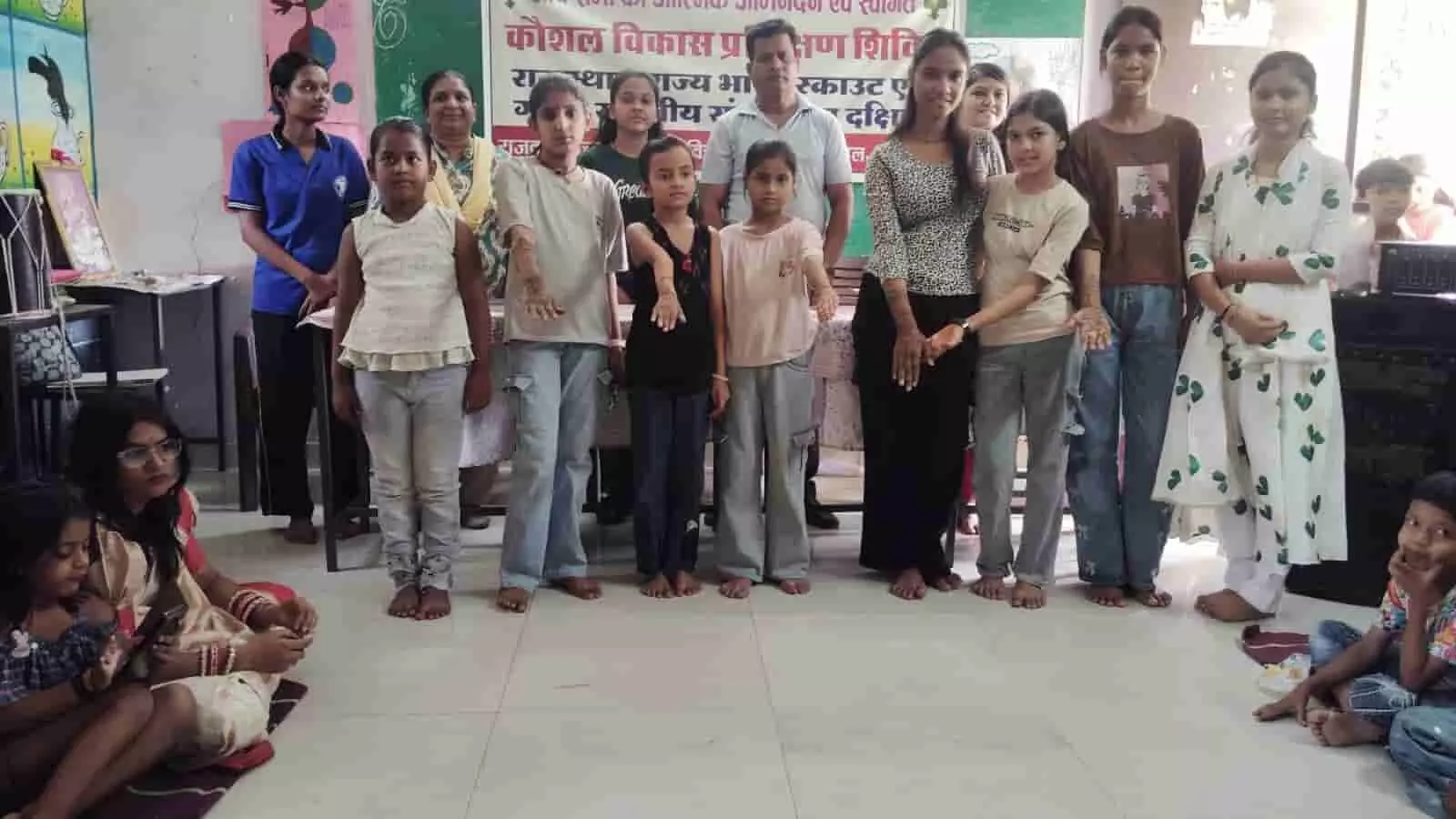 तस्वीर में एक कौशल विकास प्रशिक्षण शिविर के बैनर के सामने खड़ी कई बच्चियां अपने हाथों को आगे बढ़ाकर मेहंदी के डिजाइन दिखाती हुई नजर आ रही हैं। तस्वीर में एक कौशल विकास प्रशिक्षण शिविर के बैनर के सामने खड़ी कई बच्चियां अपने हाथों को आगे बढ़ाकर मेहंदी के डिजाइन दिखाती हुई नजर आ रही हैं।