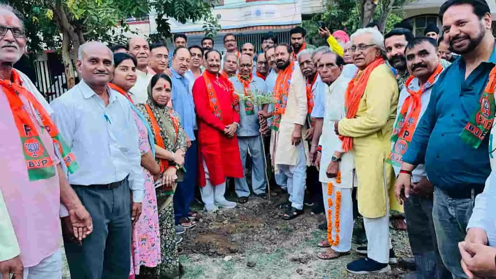 तस्वीर में केसरिया रंग के दुपट्टे (पटके) पहने कई लोग एक पार्क के भीतर नवनिर्मित गड्ढे में लगे एक छोटे पौधे के इर्द-गिर्द खड़े होकर कैमरे के सामने देख रहे हैं। तस्वीर में केसरिया रंग के दुपट्टे (पटके) पहने कई लोग एक पार्क के भीतर नवनिर्मित गड्ढे में लगे एक छोटे पौधे के इर्द-गिर्द खड़े होकर कैमरे के सामने देख रहे हैं।