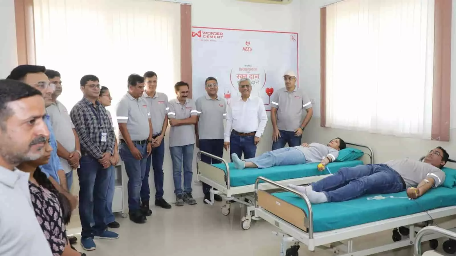 तस्वीर में एक चिकित्सालय के भीतर दो अलग-अलग बेड पर लेटे हुए एक महिला और एक पुरुष रक्तदान कर रहे हैं, जबकि वंडर सीमेंट की ग्रे टी-शर्ट पहने कई अधिकारी उनके पास खड़े नजर आ रहे हैं। तस्वीर में एक चिकित्सालय के भीतर दो अलग-अलग बेड पर लेटे हुए एक महिला और एक पुरुष रक्तदान कर रहे हैं, जबकि वंडर सीमेंट की ग्रे टी-शर्ट पहने कई अधिकारी उनके पास खड़े नजर आ रहे हैं।