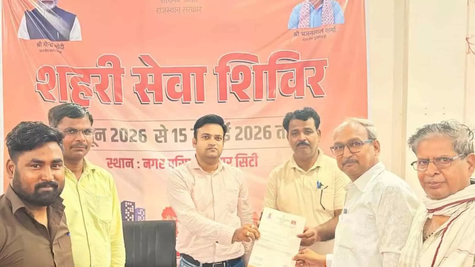 तस्वीर में शहरी सेवा शिविर लिखे एक बड़े नारंगी बैनर के सामने खड़े कुछ लोग और अधिकारी एक नागरिक को दस्तावेज़ (पट्टा) सौंपते हुए दिखाई दे रहे हैं। तस्वीर में शहरी सेवा शिविर लिखे एक बड़े नारंगी बैनर के सामने खड़े कुछ लोग और अधिकारी एक नागरिक को दस्तावेज़ (पट्टा) सौंपते हुए दिखाई दे रहे हैं।
