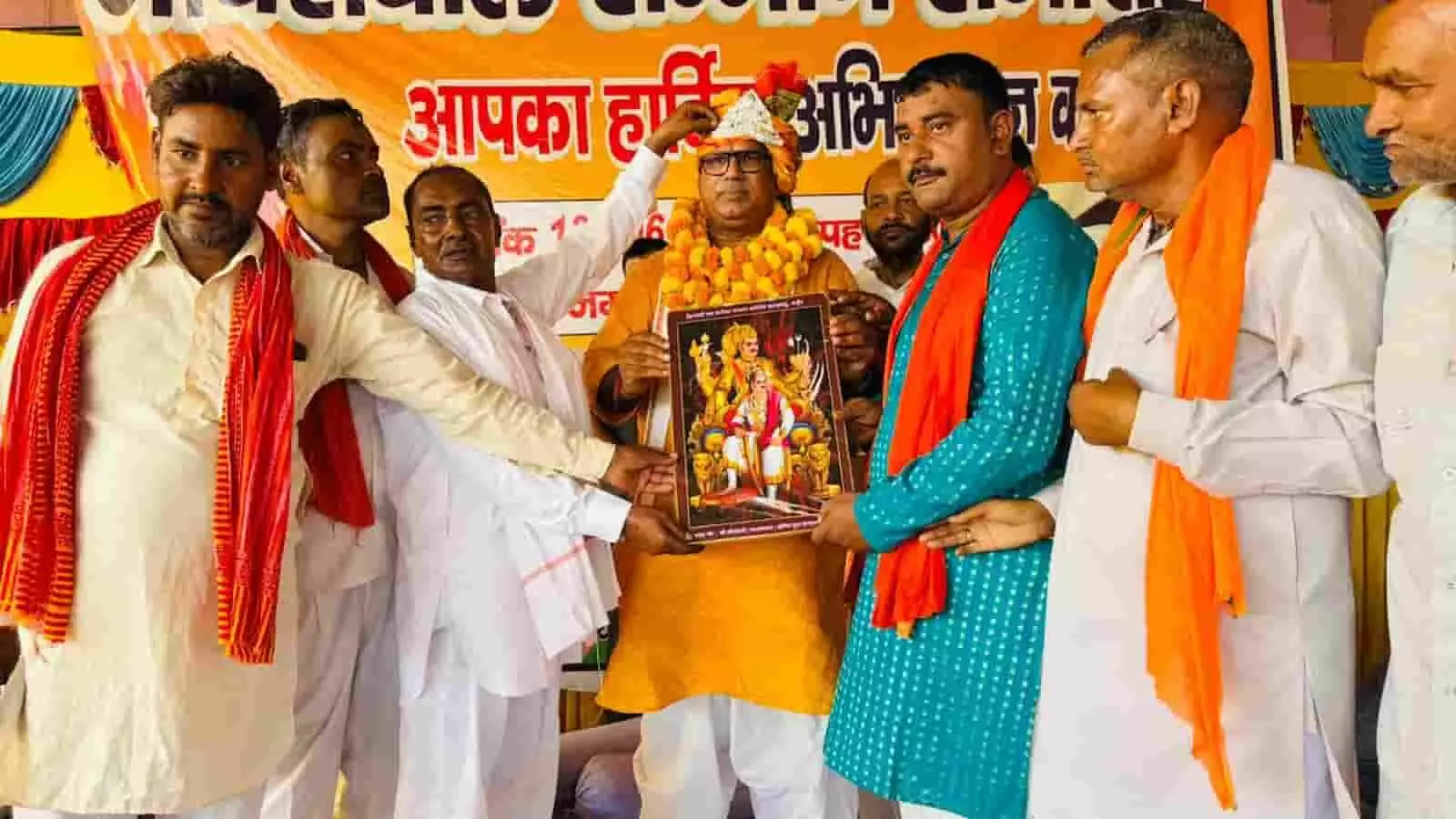 तस्वीर में एक समारोह के मंच पर पीले वस्त्र और फूलों की बड़ी माला पहने एक अतिथि (मंत्री) को कुछ लोग साफा पहना रहे हैं और उन्हें भगवान की एक फ्रेम की हुई तस्वीर भेंट कर रहे हैं। तस्वीर में एक समारोह के मंच पर पीले वस्त्र और फूलों की बड़ी माला पहने एक अतिथि (मंत्री) को कुछ लोग साफा पहना रहे हैं और उन्हें भगवान की एक फ्रेम की हुई तस्वीर भेंट कर रहे हैं।