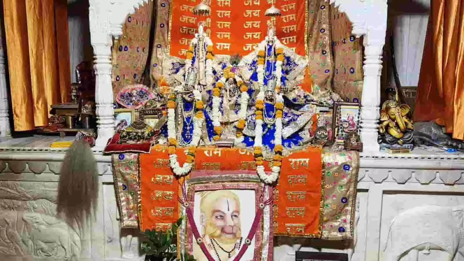 तस्वीर में एक सफेद संगमरमर के मंदिर का गर्भगृह दिख रहा है, जहां भगवान की प्रतिमाएं नीले और सुनहरे रंग के वस्त्रों तथा गेंदे के फूलों की मालाओं से सुसज्जित हैं