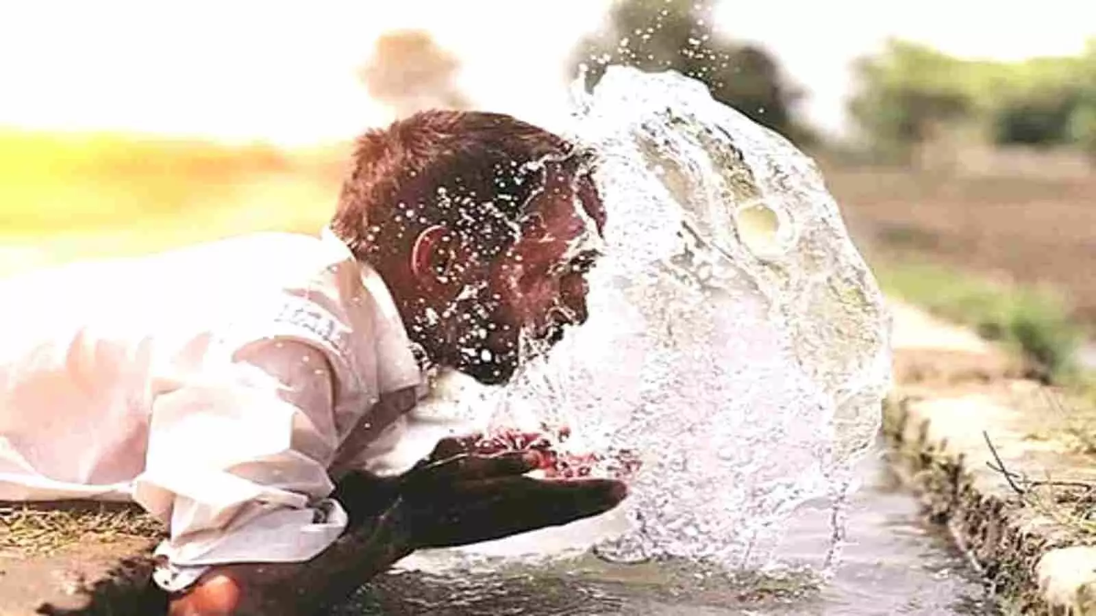 जलस्रोत के पास घुटनों के बल बैठा एक व्यक्ति अपने चेहरे पर पानी छिड़ककर गर्मी से राहत पा रहा है जलस्रोत के पास घुटनों के बल बैठा एक व्यक्ति अपने चेहरे पर पानी छिड़ककर गर्मी से राहत पा रहा है