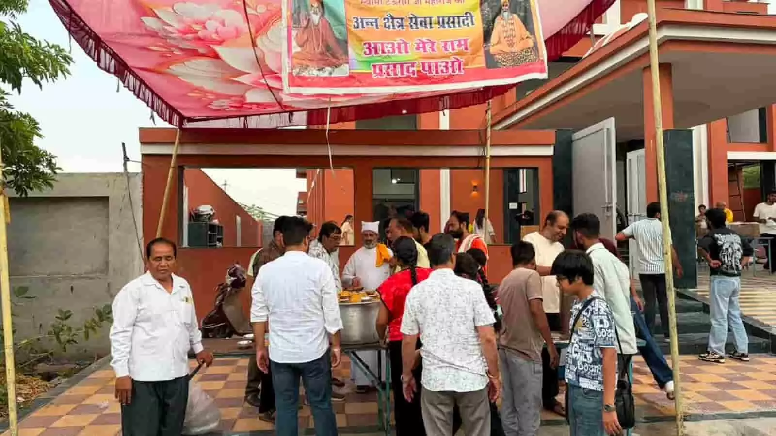 भीलवाड़ा के प्रेमप्रकाश आश्रम परिसर के बाहर टेंट के नीचे राहगीरों को प्रसाद बांटते हुए सेवादार और खड़े लोग।