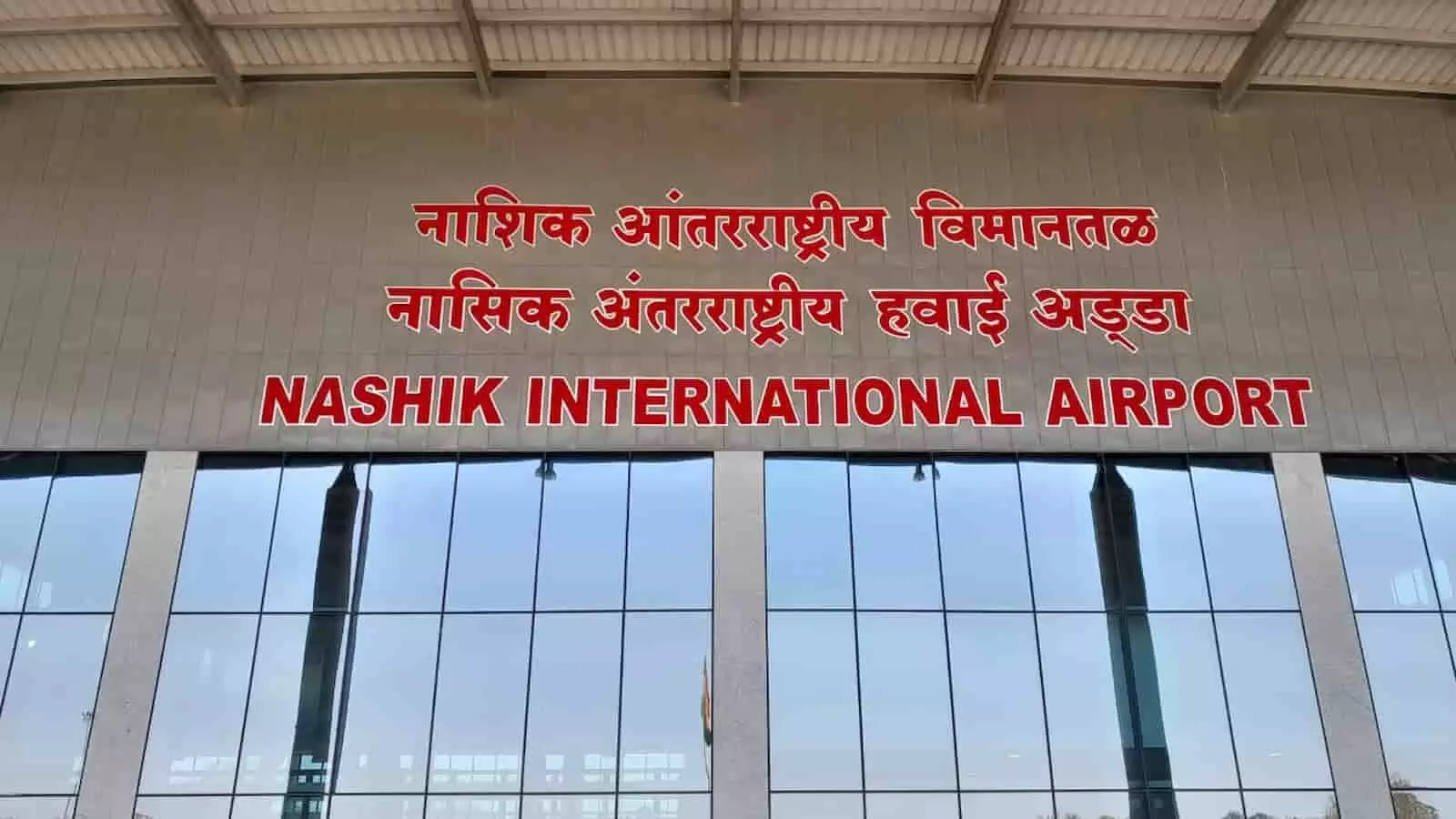 नाशिक अंतरराष्ट्रीय विमानतल के मुख्य टर्मिनल भवन का बाहरी हिस्सा और प्रवेश द्वार जहां हिंदी, मराठी और अंग्रेजी में हवाई अड्डे का नाम लिखा है। नाशिक अंतरराष्ट्रीय विमानतल के मुख्य टर्मिनल भवन का बाहरी हिस्सा और प्रवेश द्वार जहां हिंदी, मराठी और अंग्रेजी में हवाई अड्डे का नाम लिखा है।