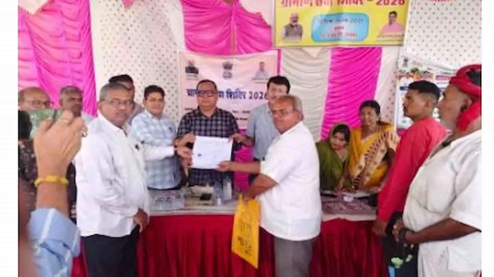 ग्रामीण सेवा शिविर के मंच पर लाभार्थी को प्रमाण पत्र वितरित करते प्रशासनिक अधिकारी।