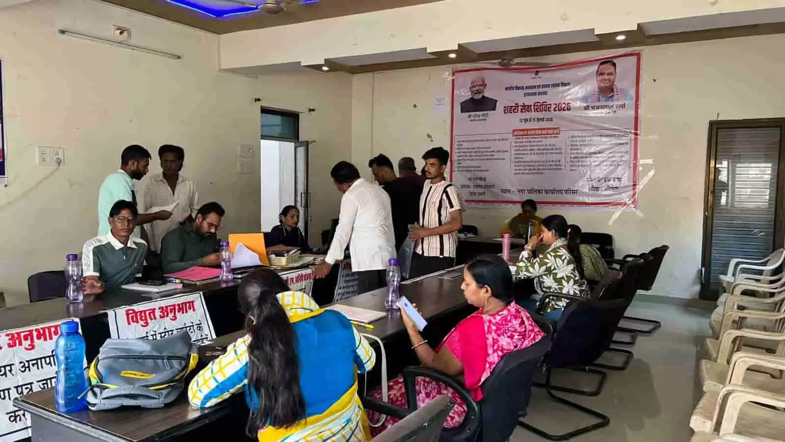 नगरपालिका परिसर में काउंटर पर बैठे अधिकारियों के समक्ष खड़े होकर अपनी फाइलों का काम करवाते नागरिक। नगरपालिका परिसर में काउंटर पर बैठे अधिकारियों के समक्ष खड़े होकर अपनी फाइलों का काम करवाते नागरिक।