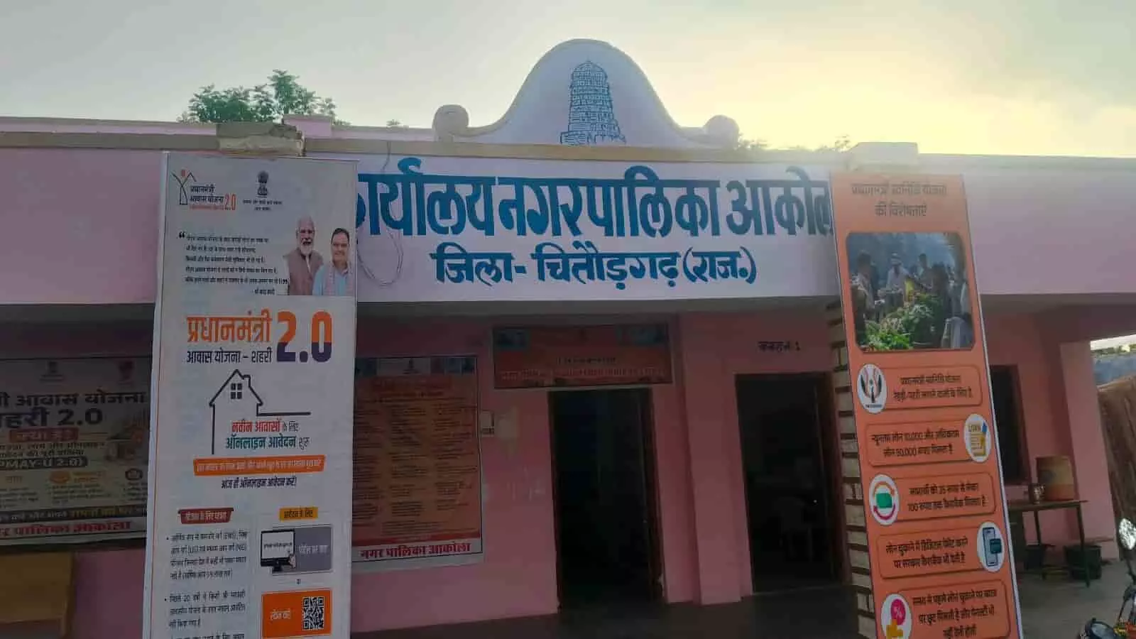 आकोला नगर पालिका कार्यालय भवन का मुख्य द्वार और सामने लगे विभिन्न सरकारी योजनाओं के प्रचार बोर्ड।