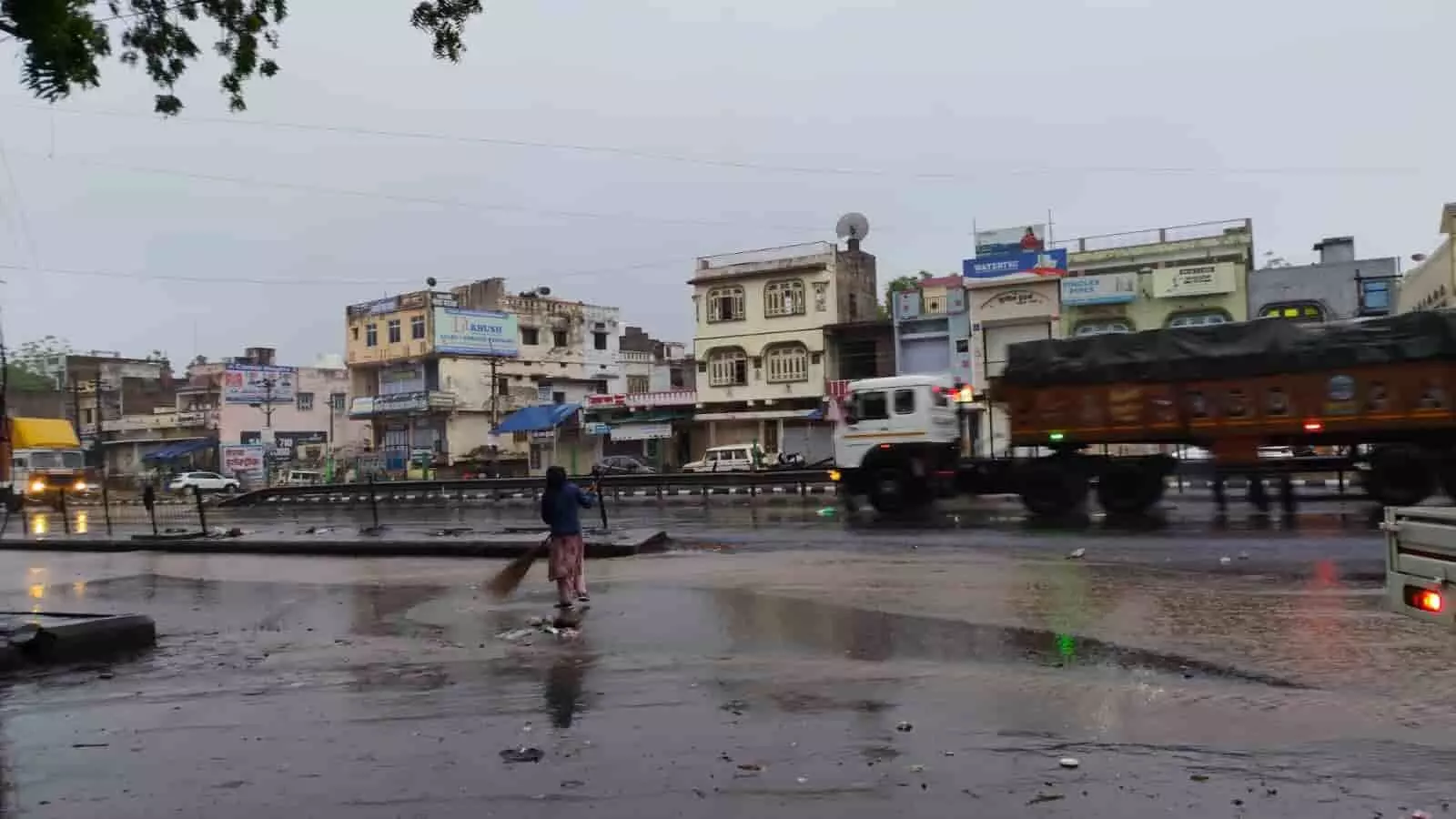 खेरवाड़ा में बारिश के बाद गीली सड़क पर झाड़ू लगाती महिला और राष्ट्रीय राजमार्ग पर चलते वाहन। खेरवाड़ा में बारिश के बाद गीली सड़क पर झाड़ू लगाती महिला और राष्ट्रीय राजमार्ग पर चलते वाहन।