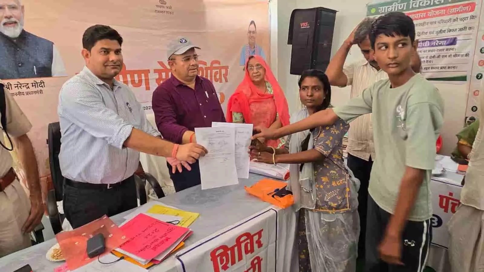 ग्रामीण सेवा शिविर में अधिकारियों द्वारा काउंटर पर आवेदकों को दस्तावेज सौंपने का दृश्य। ग्रामीण सेवा शिविर में अधिकारियों द्वारा काउंटर पर आवेदकों को दस्तावेज सौंपने का दृश्य।