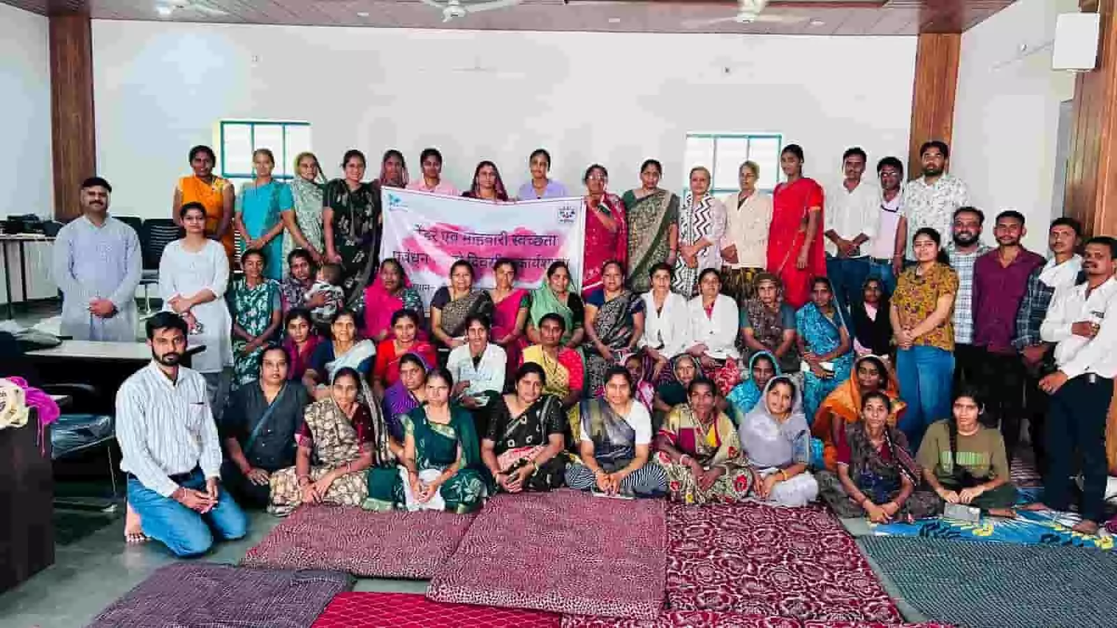 कार्यशाला के समापन पर बैनर के साथ ग्रुप फोटो के लिए बैठीं प्रशिक्षण प्राप्त प्रतिभागी महिलाएं और ट्रेनर्स।