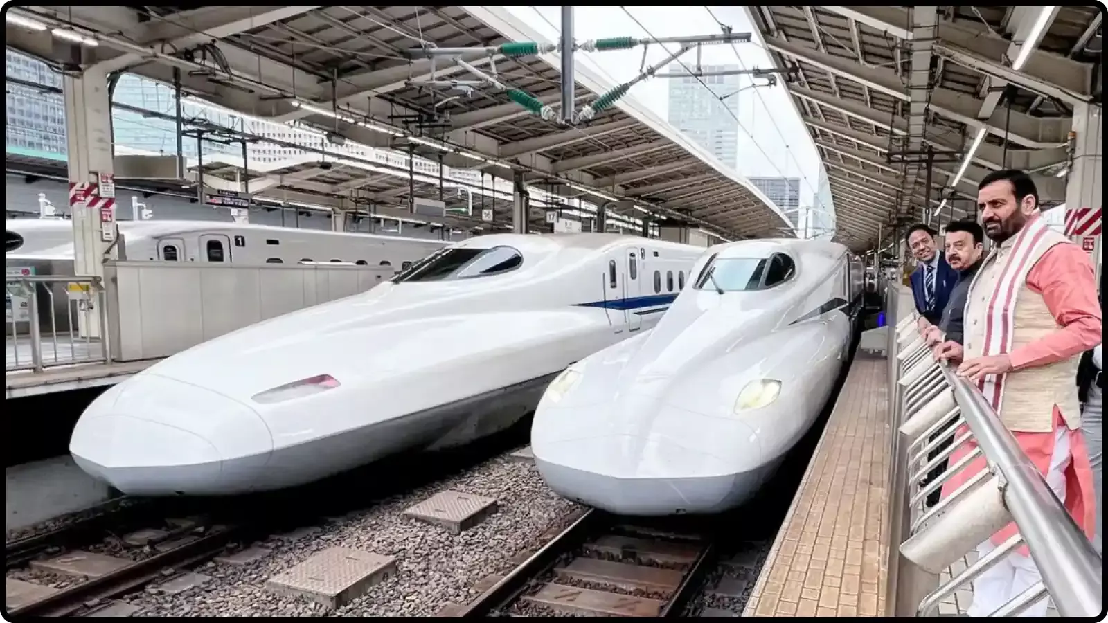 रेलवे स्टेशन के प्लेटफॉर्म पर खड़ी दो सफेद बुलेट ट्रेनें और उन्हें देखते कुछ भारतीय पुरुष यात्री। रेलवे स्टेशन के प्लेटफॉर्म पर खड़ी दो सफेद बुलेट ट्रेनें और उन्हें देखते कुछ भारतीय पुरुष यात्री।