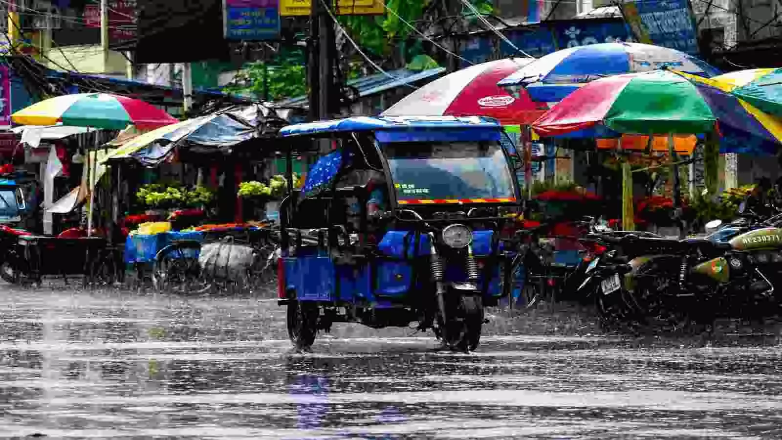 तेज बारिश में सड़क पर ई-रिक्शा और छाता लिए लोग| तेज बारिश में सड़क पर ई-रिक्शा और छाता लिए लोग|