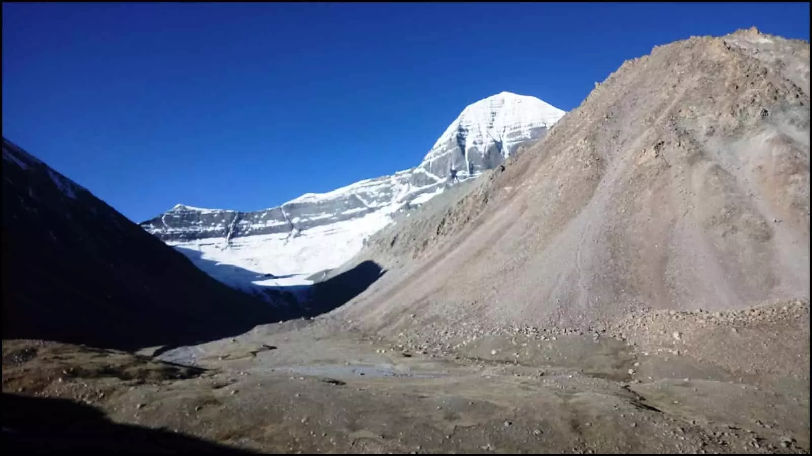 बर्फ से ढकी कैलाश पर्वत की चोटी और पथरीली घाटी तिब्बत में मानसरोवर यात्रा के मार्ग को दर्शाती है। बर्फ से ढकी कैलाश पर्वत की चोटी और पथरीली घाटी तिब्बत में मानसरोवर यात्रा के मार्ग को दर्शाती है।