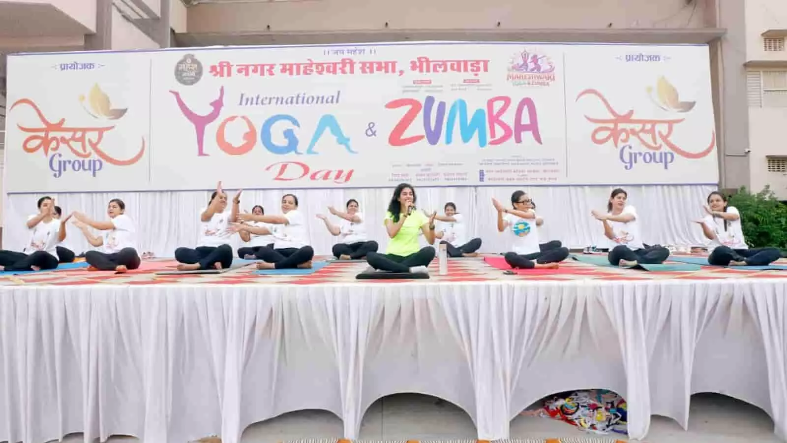महेश शिक्षा सदन भीलवाड़ा के मंच पर अंतर्राष्ट्रीय योग दिवस पर योगाभ्यास करतीं प्रशिक्षक और महिला प्रतिभागी।