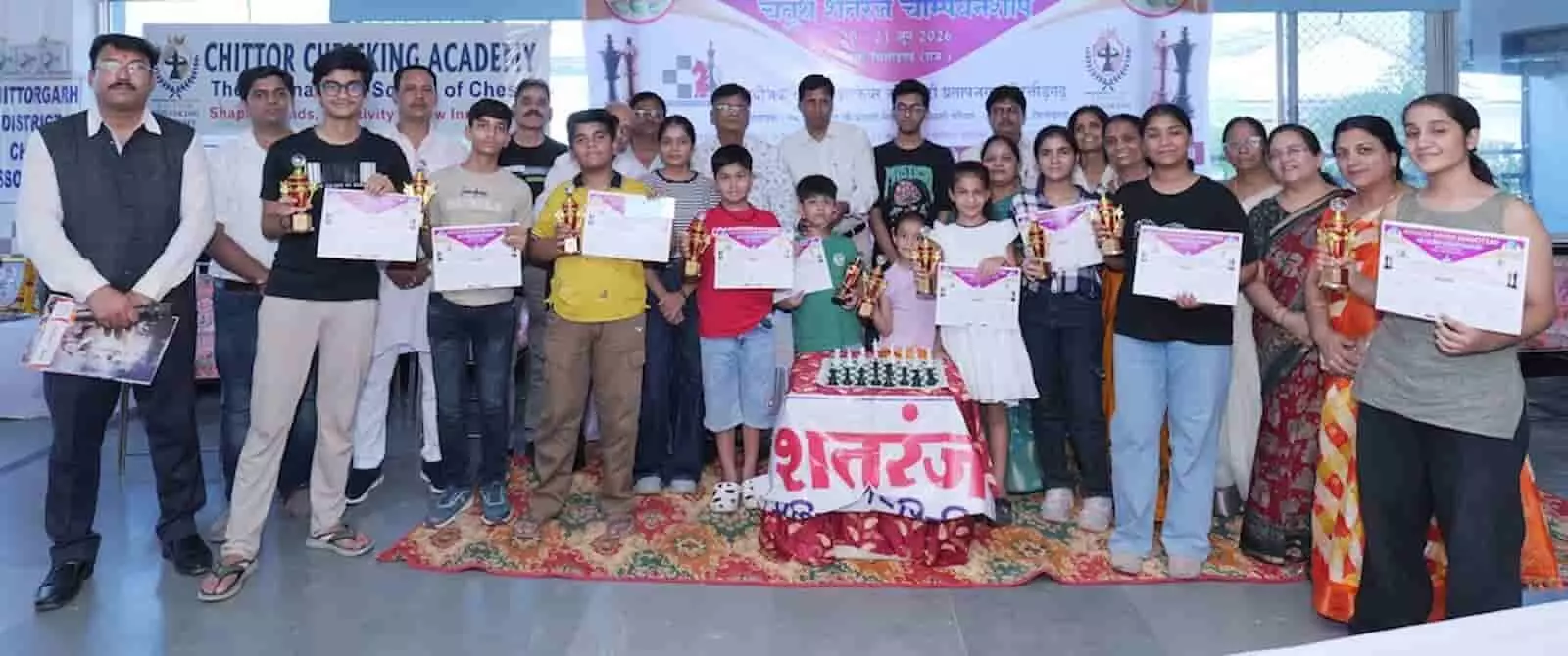 चित्तौड़गढ़ में आयोजित शतरंज चैम्पियनशिप के समापन समारोह में ट्रॉफी और सर्टिफिकेट के साथ मंच पर खड़े विजेता प्रतिभागी और अतिथि।