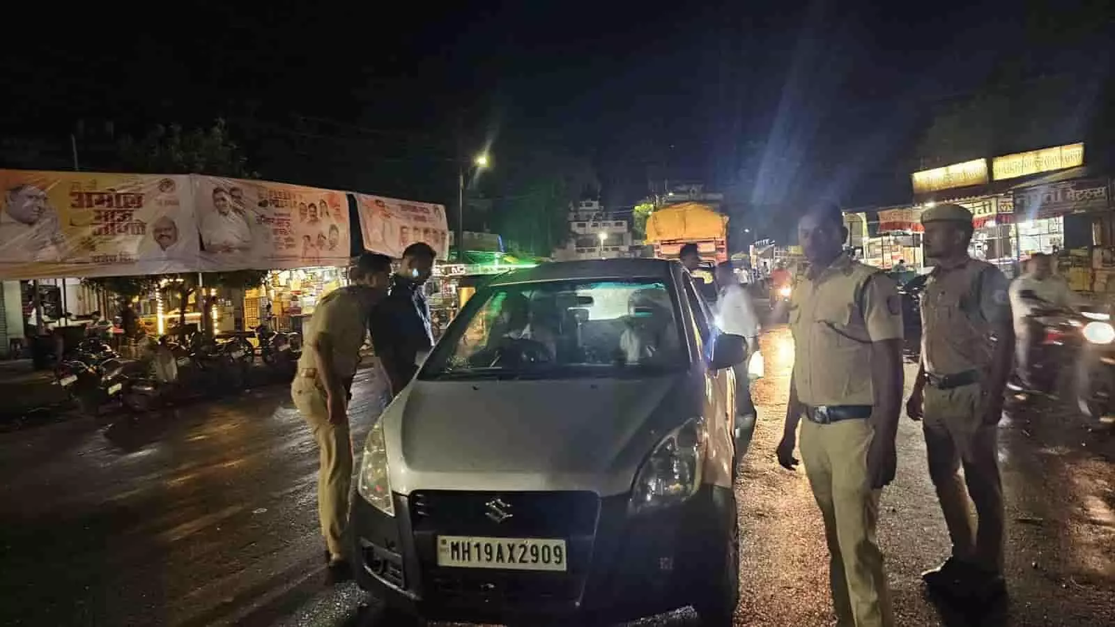 रात के समय सड़क पर कार रोककर जांच करते पुलिसकर्मी और खड़े अधिकारी।