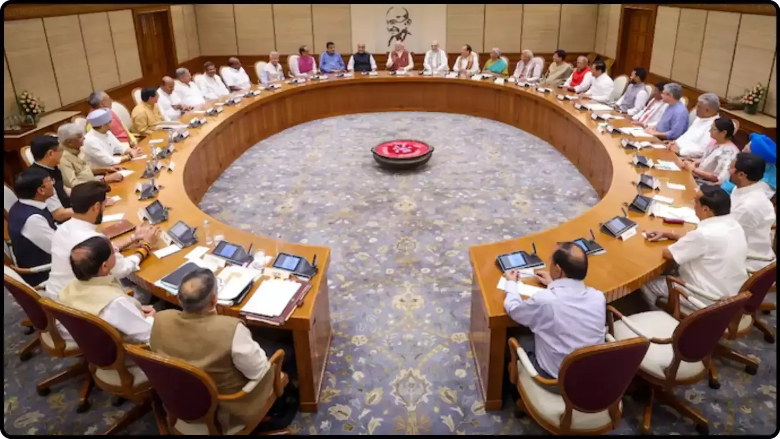एक बड़ी गोलाकार मेज के चारों ओर बैठे हुए मंत्रीगण दिल्ली में कैबिनेट बैठक के संदर्भ में दिख रहे हैं।