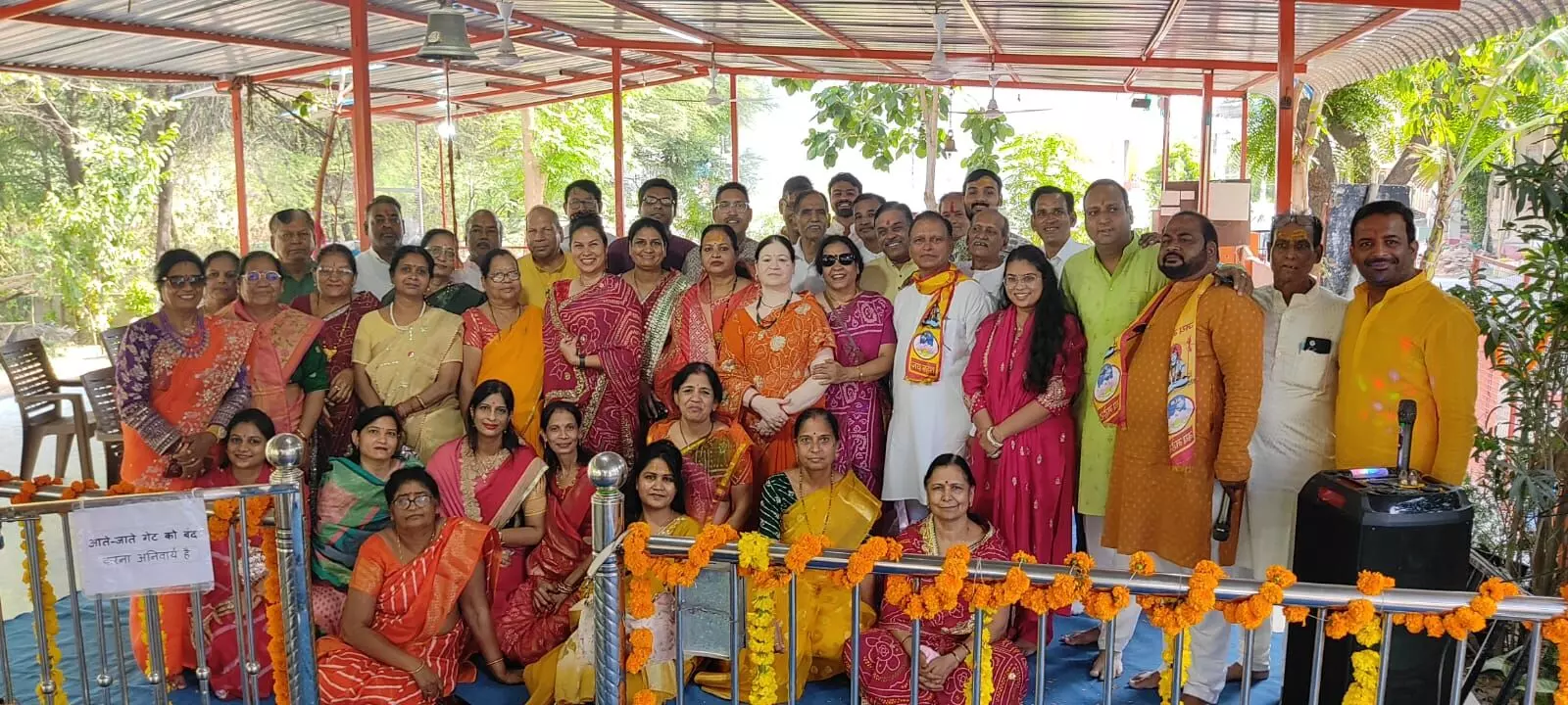 मंदिर परिसर में खड़े और बैठे पुरुषों व महिलाओं का बड़ा समूह सामूहिक फोटो के लिए पोज देता हुआ, सामने फूलों से सजी रेलिंग दिखाई दे रही है।