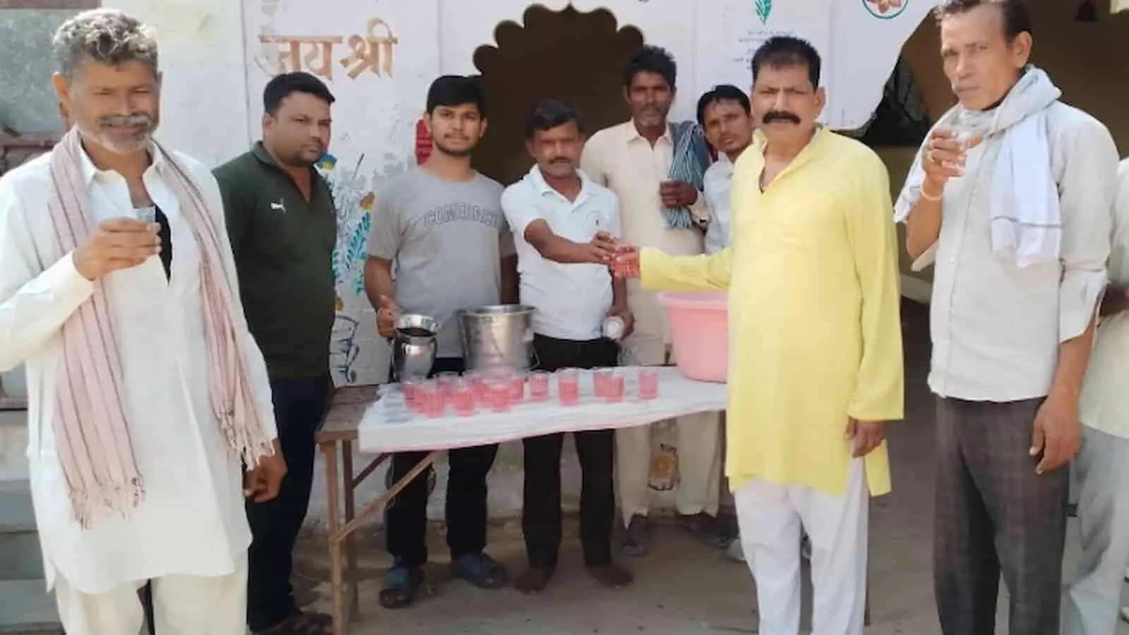 मेज पर रखे शरबत के पास खड़े पुरुष इमारत के बाहर सेवा कार्य में। मेज पर रखे शरबत के पास खड़े पुरुष इमारत के बाहर सेवा कार्य में।