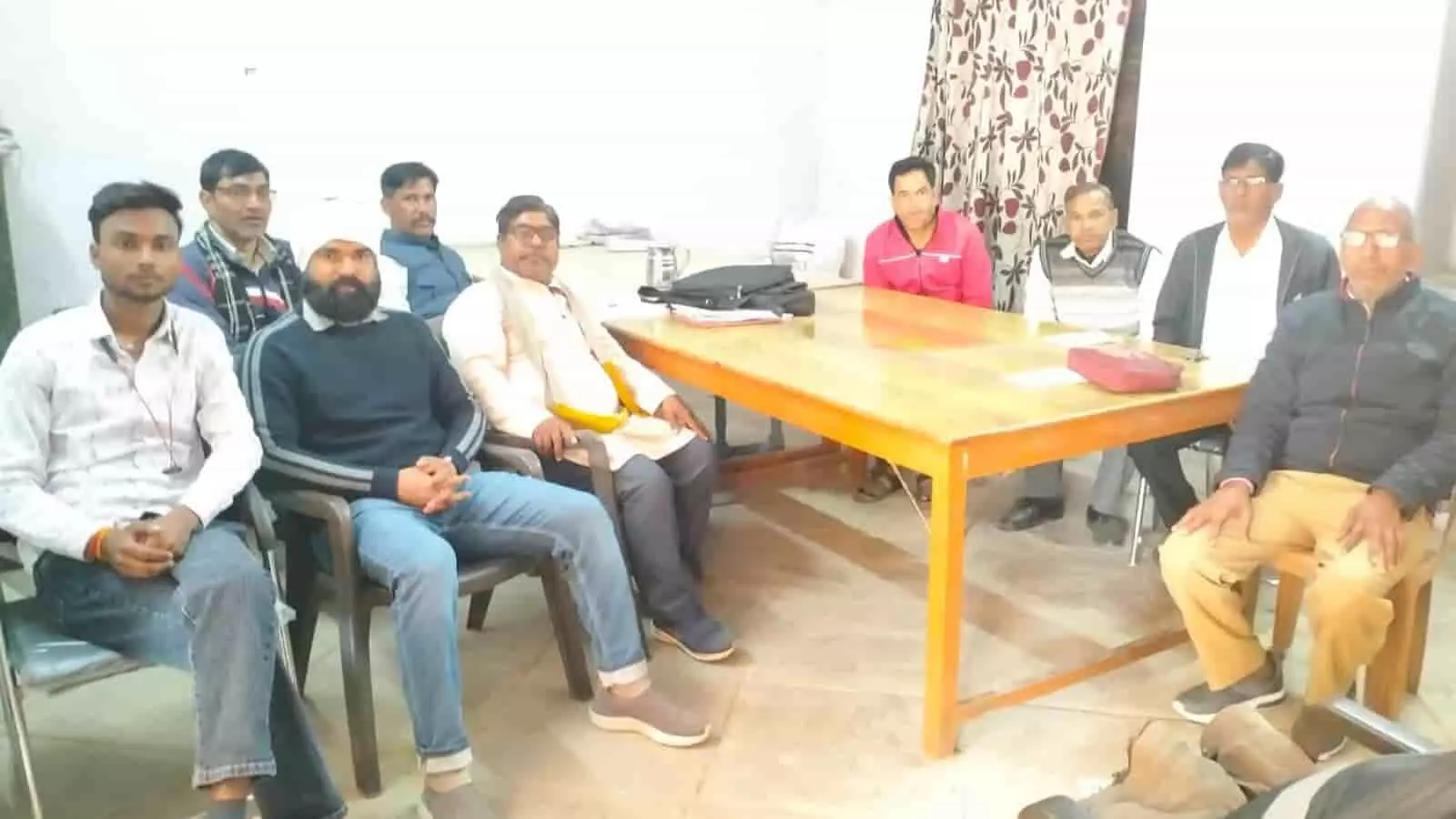 कमरे में लकड़ी की मेज के चारों ओर कुर्सियों पर बैठे पुरुष शिक्षक संघ की बैठक के दौरान। कमरे में लकड़ी की मेज के चारों ओर कुर्सियों पर बैठे पुरुष शिक्षक संघ की बैठक के दौरान।