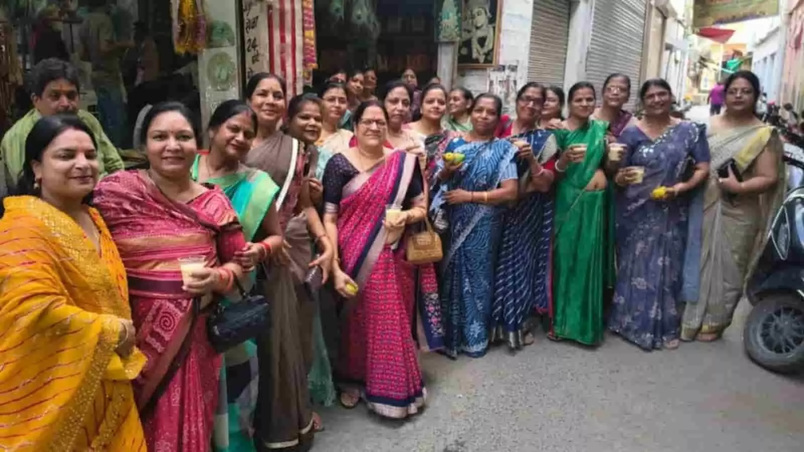 साड़ियों में महिलाएं मंदिर के बाहर हाथ में शरबत के गिलास और आम लिए खड़ी हैं। साड़ियों में महिलाएं मंदिर के बाहर हाथ में शरबत के गिलास और आम लिए खड़ी हैं।