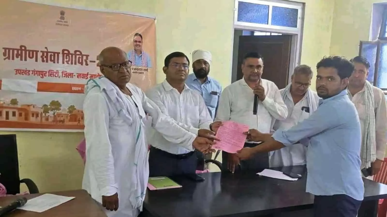 ग्रामीण सेवा शिविर में अधिकारी एक व्यक्ति को गुलाबी पट्टा सौंपते हुए दस्तावेज वितरण के दौरान। ग्रामीण सेवा शिविर में अधिकारी एक व्यक्ति को गुलाबी पट्टा सौंपते हुए दस्तावेज वितरण के दौरान।