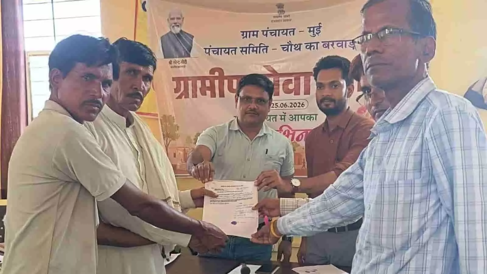 मेज के पास खड़े पुरुष मुई पंचायत शिविर में आधिकारिक दस्तावेज थामे हुए। मेज के पास खड़े पुरुष मुई पंचायत शिविर में आधिकारिक दस्तावेज थामे हुए।