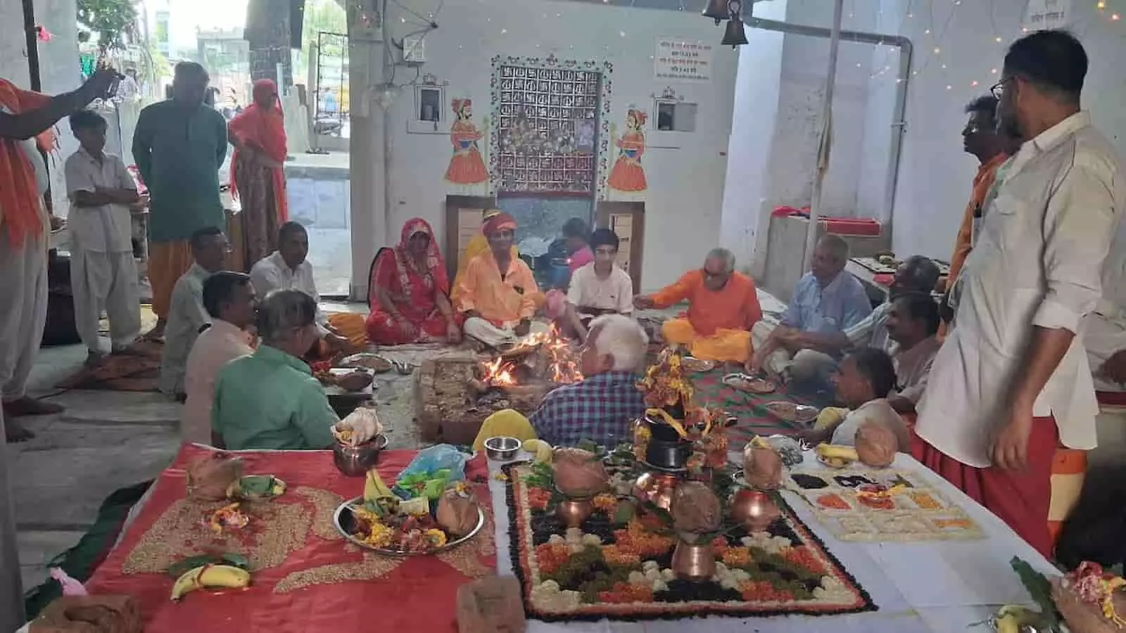 मन्दिर परिसर में हवन कुंड के पास बैठकर धार्मिक अनुष्ठान करते श्रद्धालु और रखी हुई पूजन सामग्री।