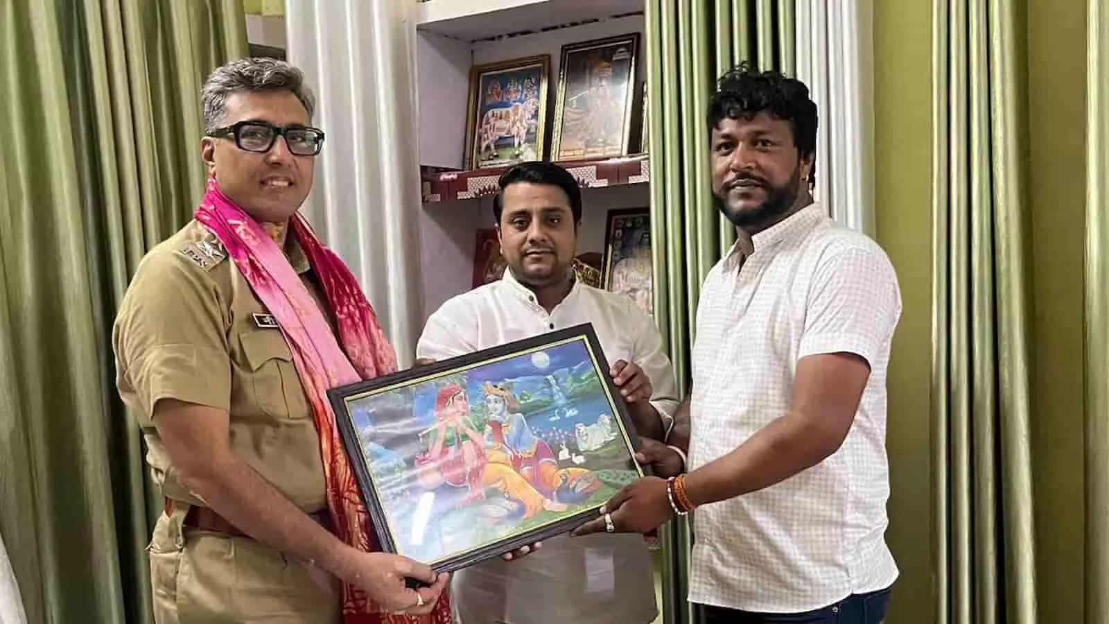 पुलिस अधिकारी को कृष्ण-राधा की तस्वीर भेंट करते हुए तीन पुरुष कमरे में।