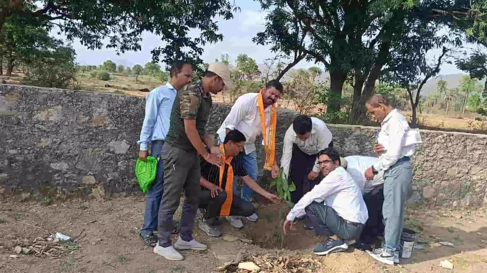 : ग्रामीण सेवा शिविर में अधिकारियों द्वारा गड्ढे में पौधा लगाकर वृक्षारोपण करने का दृश्य।