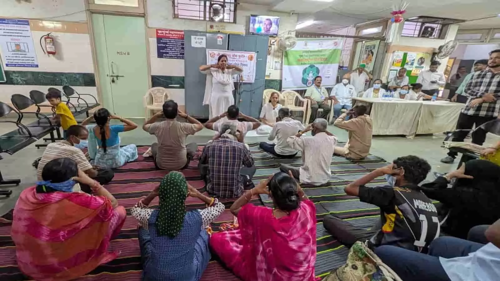 : सभागार में योग प्रशिक्षिका के निर्देशन में दरी पर बैठकर योगाभ्यास करते हुए विभिन्न नागरिक। : सभागार में योग प्रशिक्षिका के निर्देशन में दरी पर बैठकर योगाभ्यास करते हुए विभिन्न नागरिक।