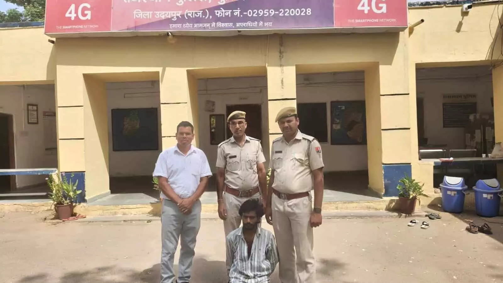 झाड़ोल पुलिस थाने के बाहर पुलिसकर्मियों की गिरफ्त में बैठा हुआ एक युवक।