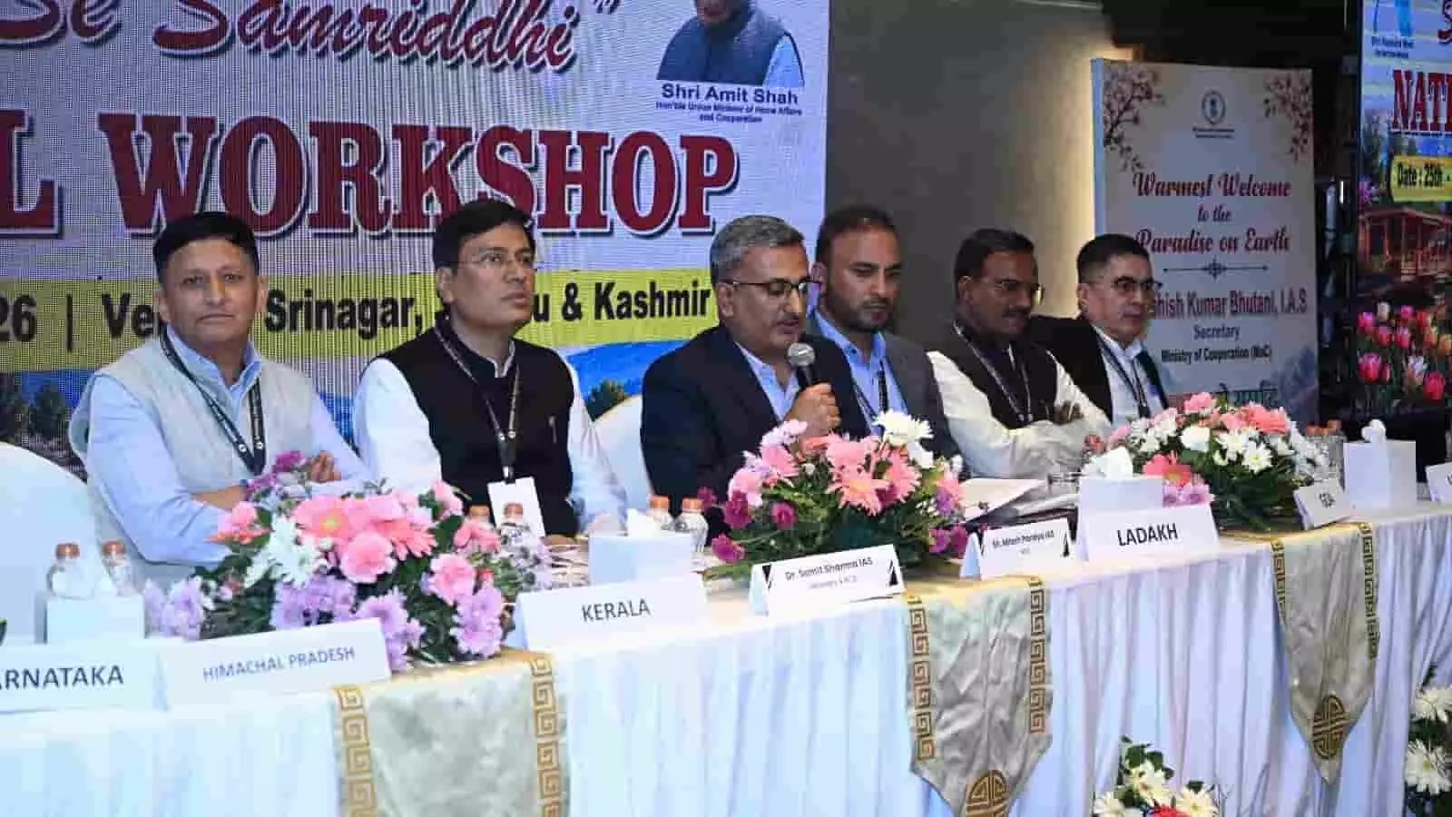 राष्ट्रीय सहकारिता कार्यशाला के मंच पर चर्चा करते अधिकारी और विभिन्न राज्यों के नाम की नेमप्लेट।