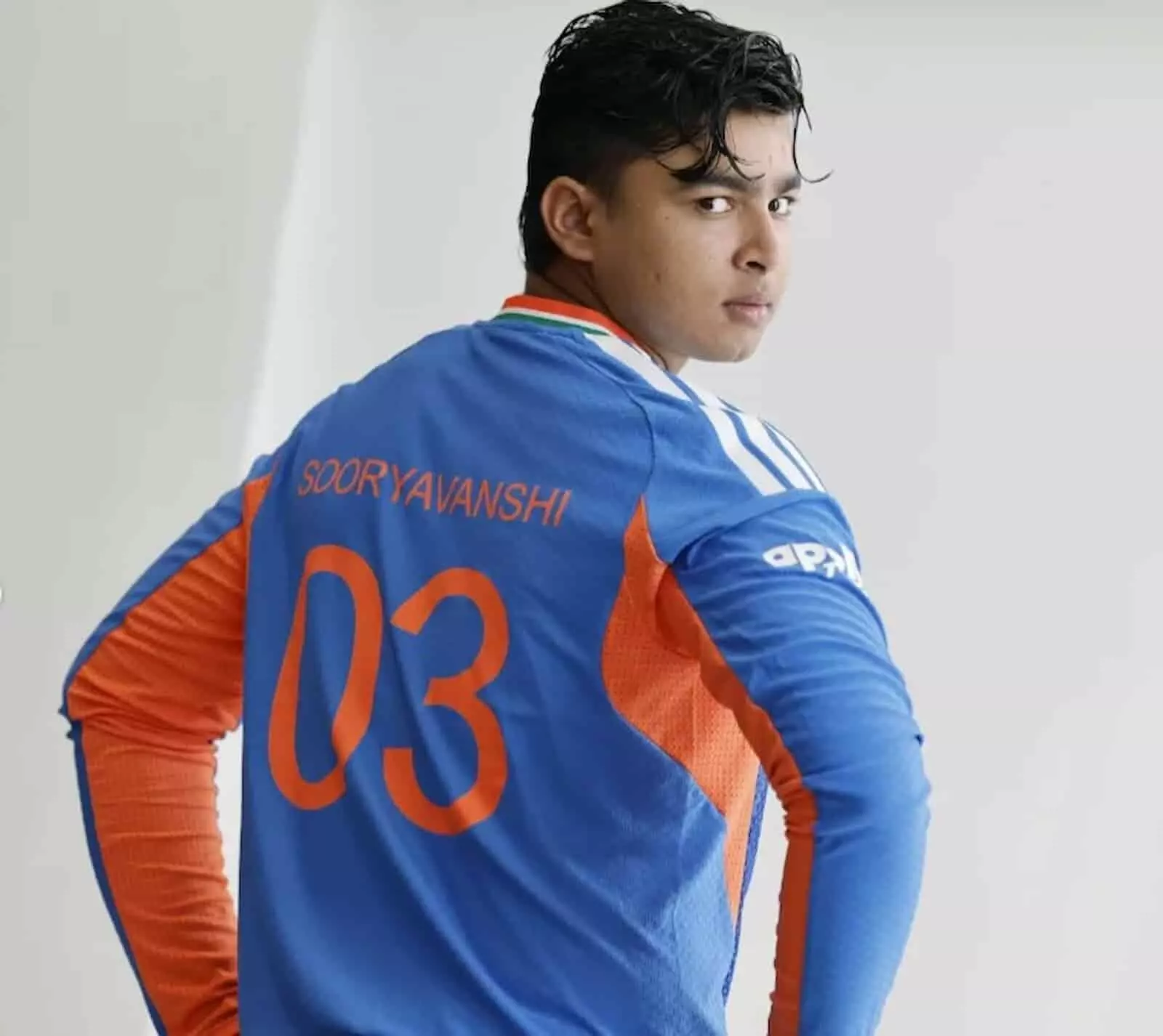 तस्वीर में भारतीय क्रिकेटर वैभव सूर्यवंशी नीली टीम जर्सी पहने हुए पीछे देख रहे हैं।