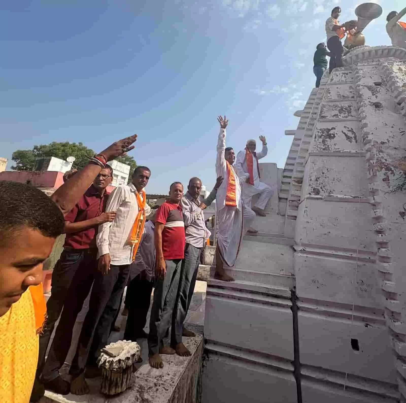 मंदिर के शिखर पर ध्वजा चढ़ाते भक्त और प्रांगण में खड़े श्रद्धालु। मंदिर के शिखर पर ध्वजा चढ़ाते भक्त और प्रांगण में खड़े श्रद्धालु।