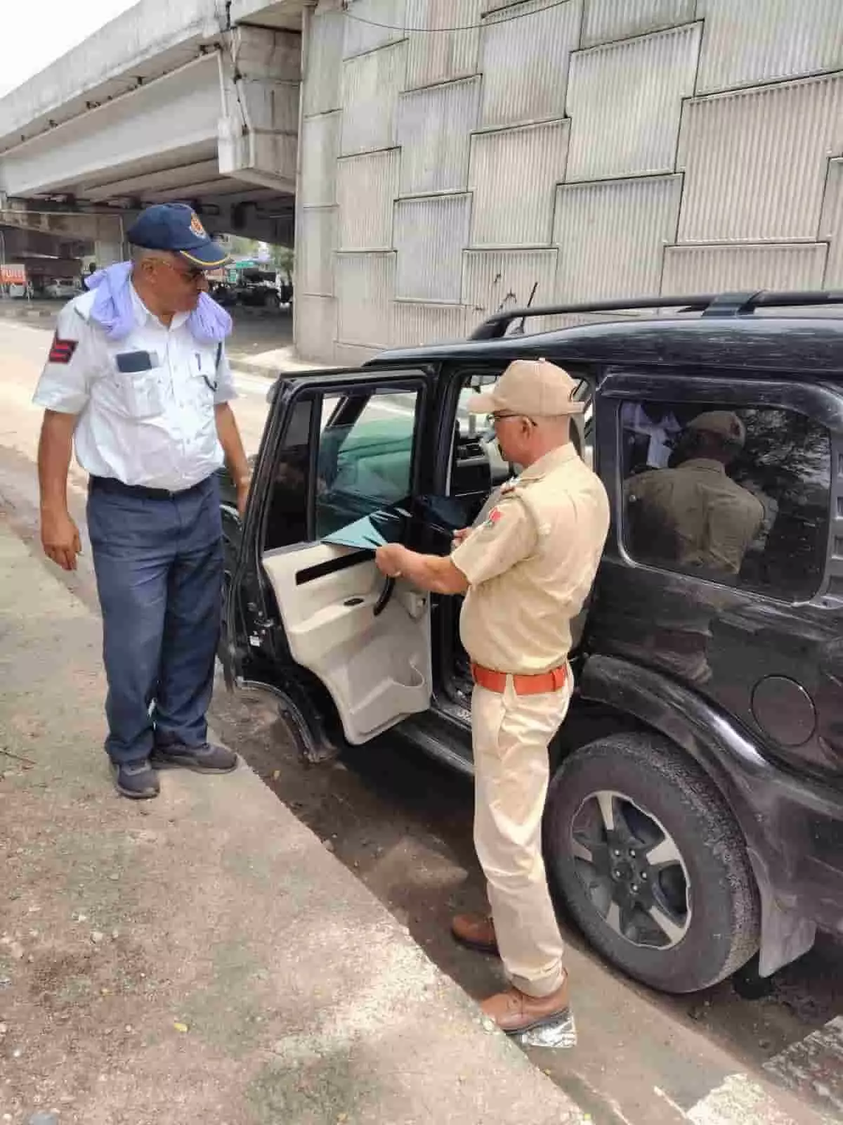 सड़क किनारे एक ट्रैफिक पुलिस अधिकारी कार से अवैध काली फिल्म हटा रहे हैं।