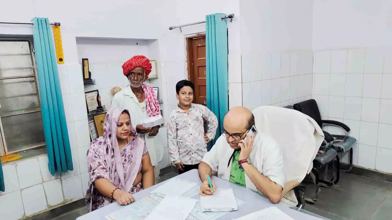 उपजिला चिकित्सालय में फोन पर बात करते डॉक्टर और परामर्श के लिए बैठे ग्रामीण मरीज।
