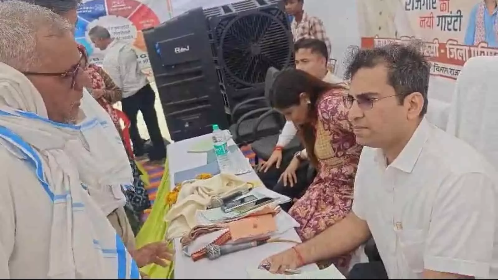 तस्वीर में ग्रामीण सेवा शिविर के दौरान स्टॉल पर बैठे अधिकारी से बात करता बुजुर्ग व्यक्ति दिख रहा है। तस्वीर में ग्रामीण सेवा शिविर के दौरान स्टॉल पर बैठे अधिकारी से बात करता बुजुर्ग व्यक्ति दिख रहा है।